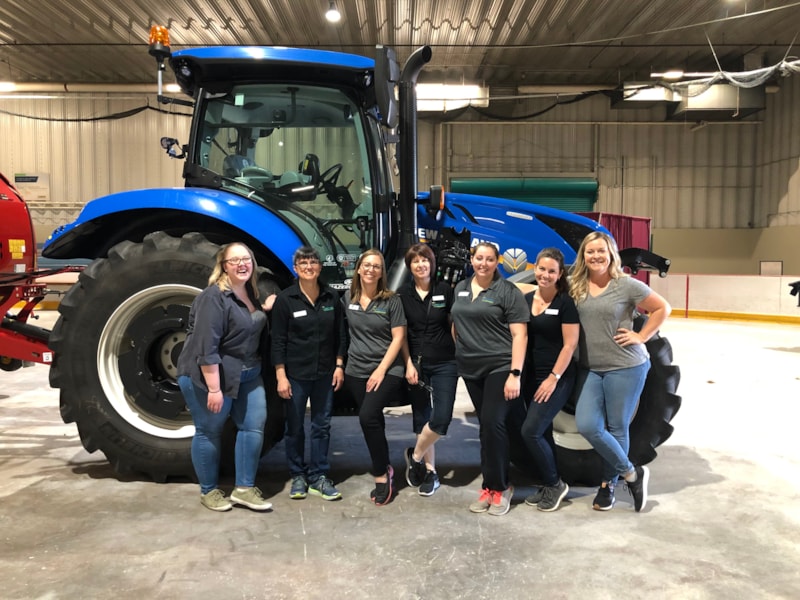 Employees smiling and standing in front of blue tractor