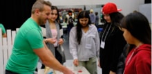 Volunteer working with four students at a Career Expo station on strawberry DNA